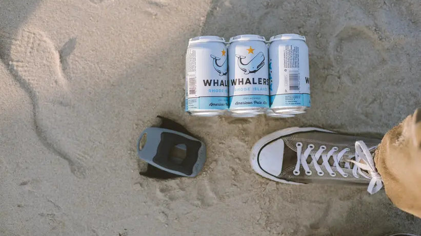Draft Top Lift in sand next to three beer cans and a person is standing near