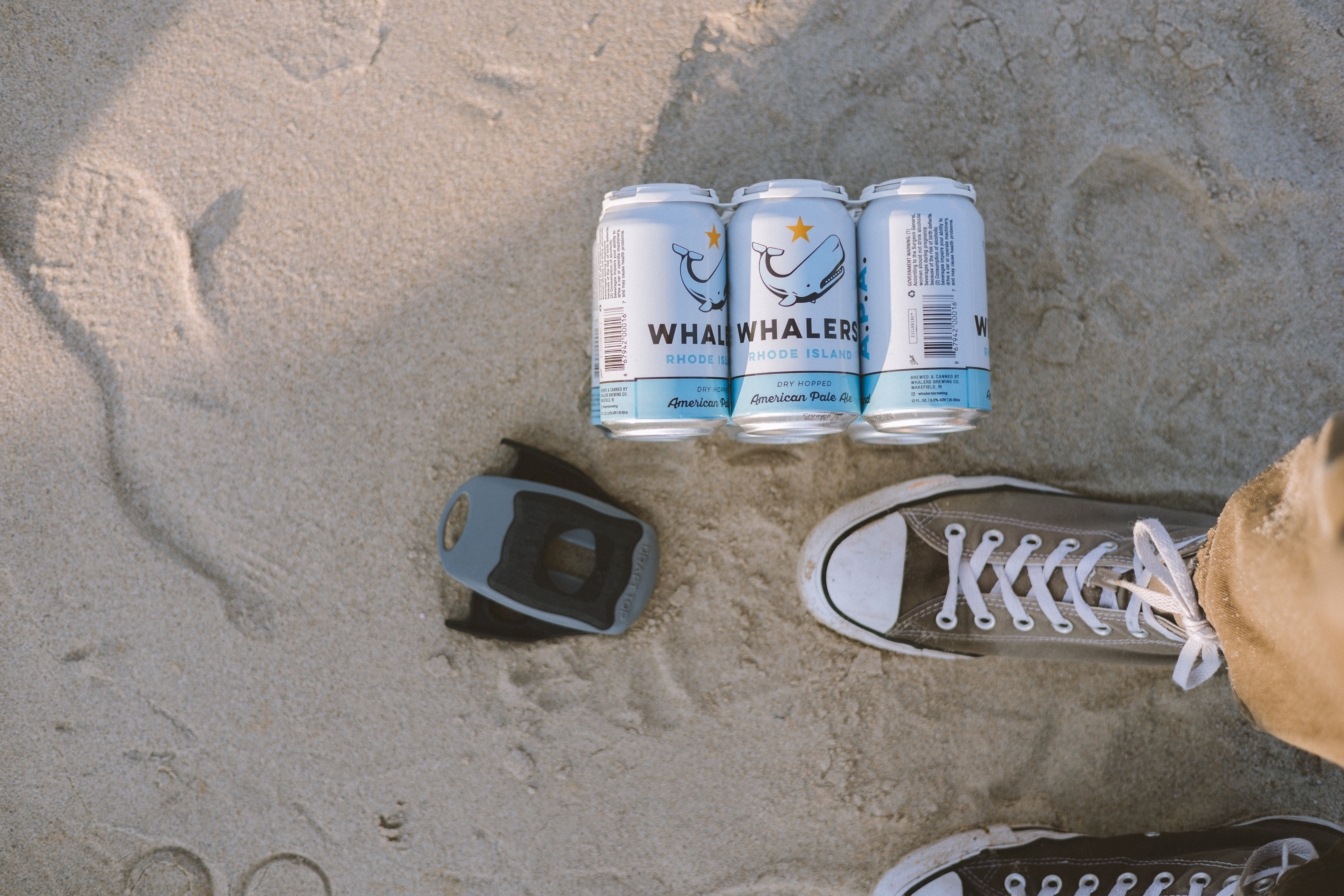 Draft Top Lift in sand next to three beer cans and a person is standing near 